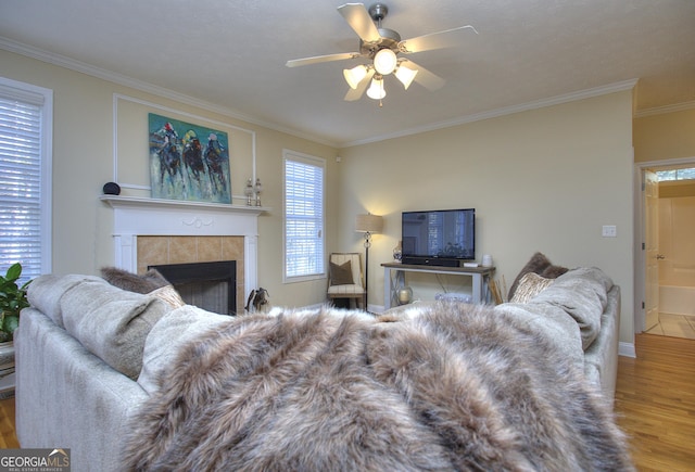 living room featuring a tile fireplace, wood-type flooring, ceiling fan, and ornamental molding