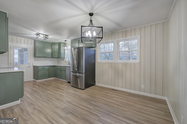 kitchen with a healthy amount of sunlight, green cabinets, light hardwood / wood-style floors, decorative backsplash, and appliances with stainless steel finishes