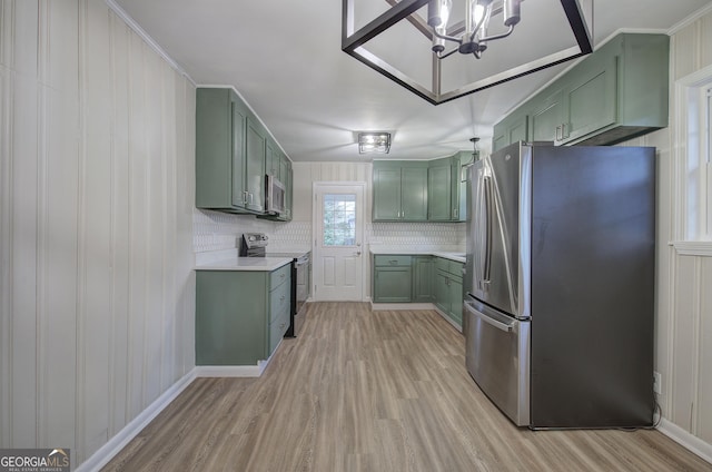 kitchen featuring backsplash, green cabinets, appliances with stainless steel finishes, a notable chandelier, and light hardwood / wood-style floors