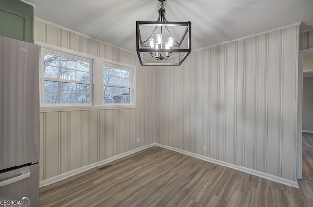 unfurnished dining area featuring hardwood / wood-style flooring, a notable chandelier, and crown molding