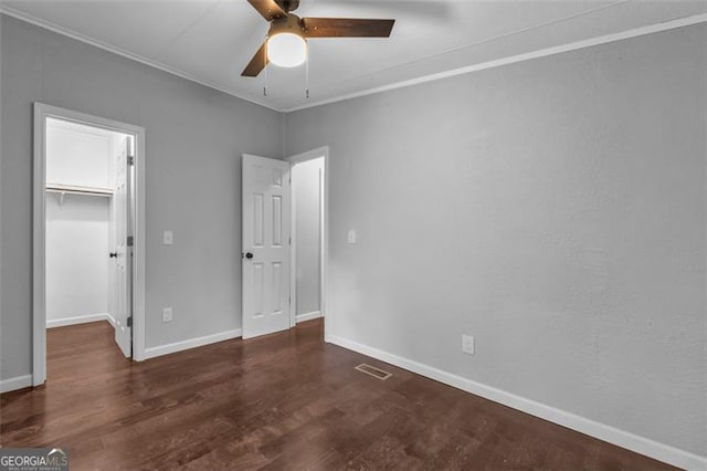 unfurnished bedroom with a walk in closet, ornamental molding, ceiling fan, dark hardwood / wood-style floors, and a closet