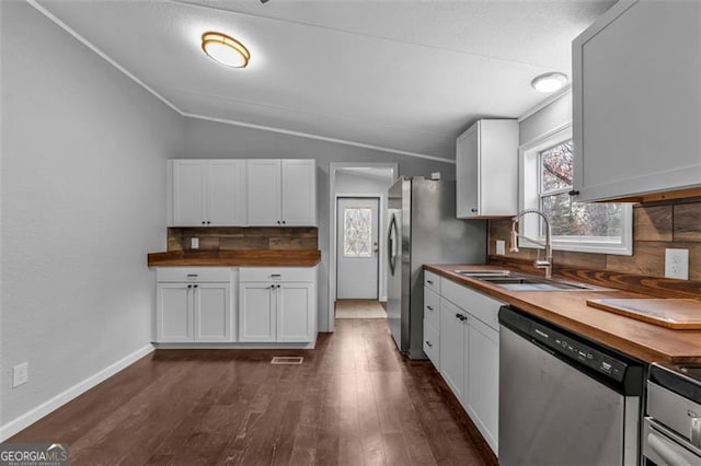 kitchen featuring butcher block counters, sink, vaulted ceiling, appliances with stainless steel finishes, and white cabinetry