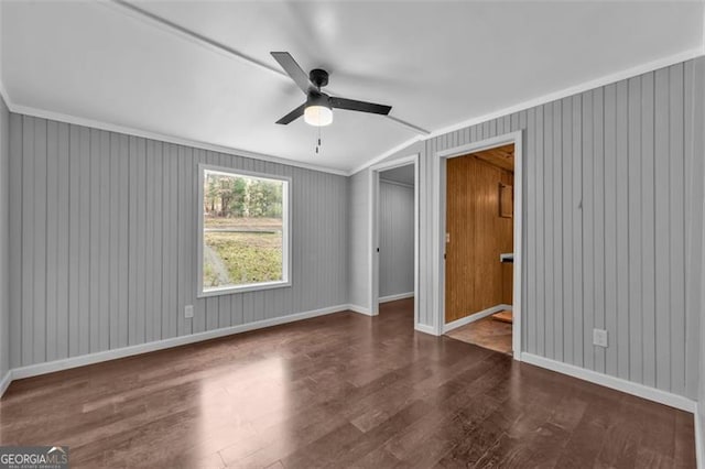 unfurnished bedroom with ceiling fan, crown molding, dark wood-type flooring, and wooden walls