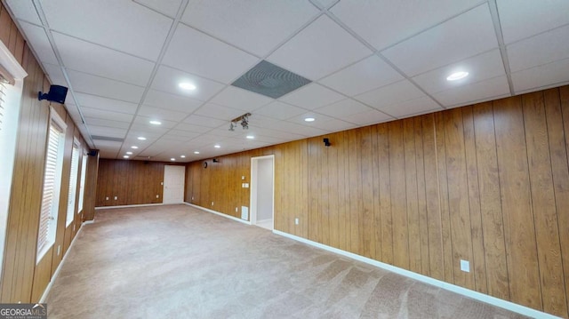 carpeted spare room featuring a paneled ceiling and wood walls