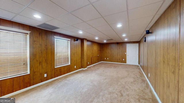 basement with a paneled ceiling, wood walls, and light carpet