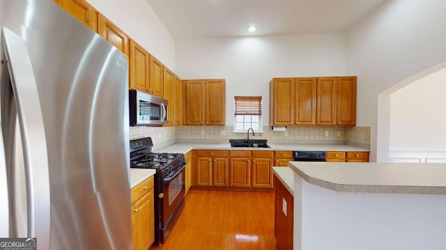 kitchen featuring black appliances, backsplash, light hardwood / wood-style floors, and sink