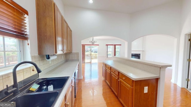 kitchen featuring decorative backsplash, sink, light hardwood / wood-style flooring, a chandelier, and a high ceiling