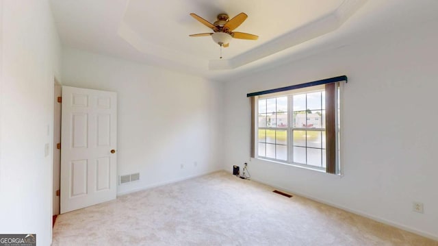 carpeted spare room with a tray ceiling and ceiling fan