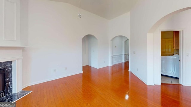 unfurnished living room with hardwood / wood-style floors, high vaulted ceiling, washer / clothes dryer, and a high end fireplace