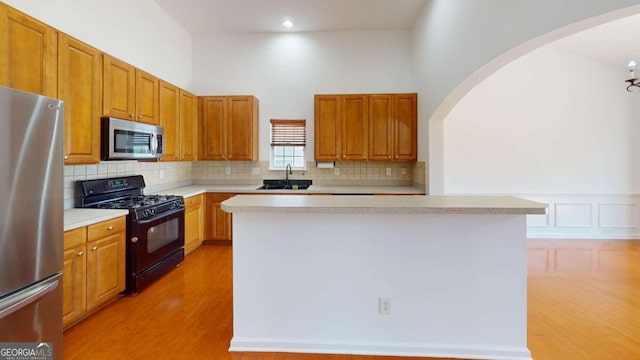 kitchen with sink, a kitchen island, stainless steel appliances, and light wood-type flooring