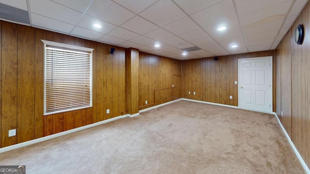 basement with light carpet, a paneled ceiling, and wooden walls