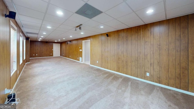 empty room featuring wood walls, a drop ceiling, and carpet floors