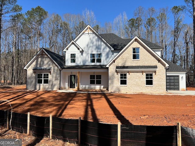 view of front of house with a garage, roof with shingles, fence, and brick siding