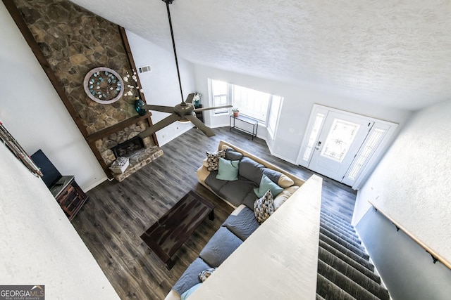 living room featuring ceiling fan, dark wood-type flooring, a stone fireplace, and a textured ceiling