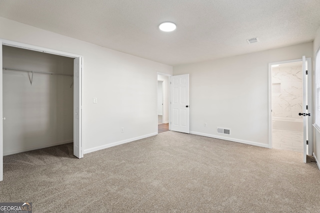 unfurnished bedroom with carpet flooring, a textured ceiling, ensuite bathroom, and a closet