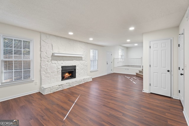 unfurnished living room featuring a stone fireplace, dark hardwood / wood-style flooring, and a textured ceiling