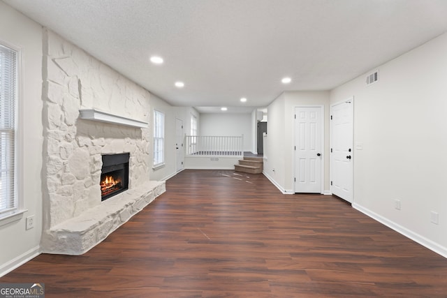 unfurnished living room with a textured ceiling, a stone fireplace, and dark hardwood / wood-style floors