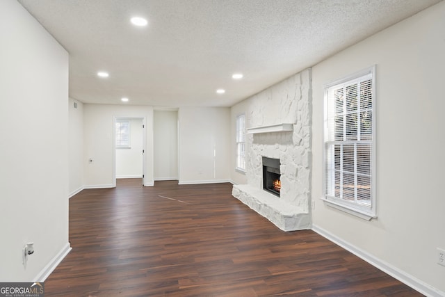 unfurnished living room featuring a stone fireplace, dark hardwood / wood-style flooring, and a textured ceiling