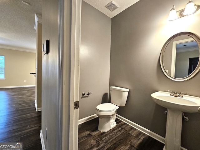 bathroom with wood-type flooring, a textured ceiling, toilet, and crown molding