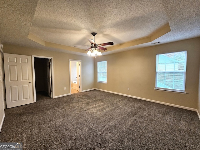 unfurnished bedroom featuring ensuite bathroom, ceiling fan, a raised ceiling, and a spacious closet