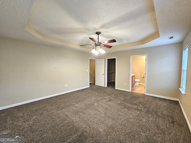 unfurnished bedroom featuring ensuite bathroom, ceiling fan, a spacious closet, a tray ceiling, and a closet