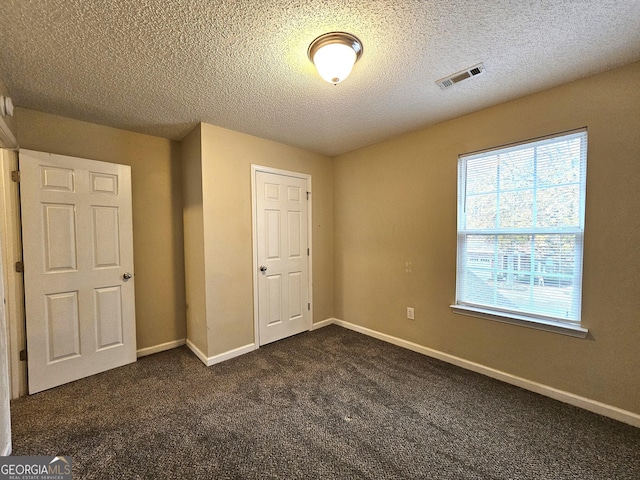 unfurnished bedroom with a closet, dark carpet, and a textured ceiling