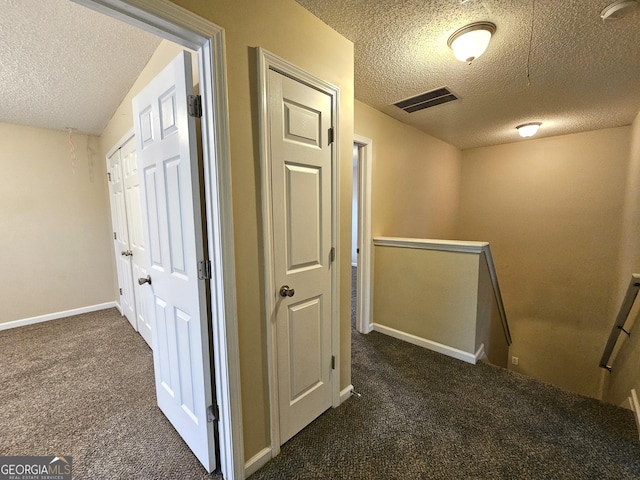 hallway featuring dark carpet and a textured ceiling