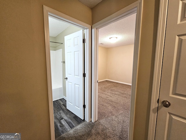 hall with a textured ceiling and dark colored carpet