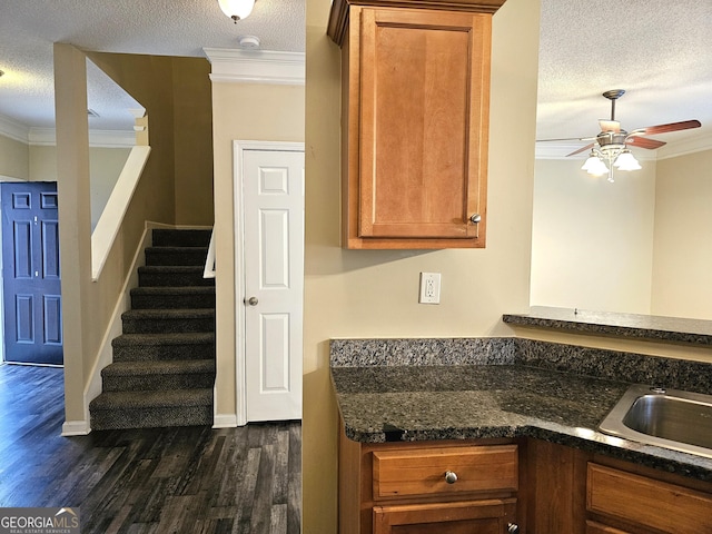 kitchen featuring a textured ceiling, ceiling fan, dark wood-type flooring, crown molding, and dark stone countertops