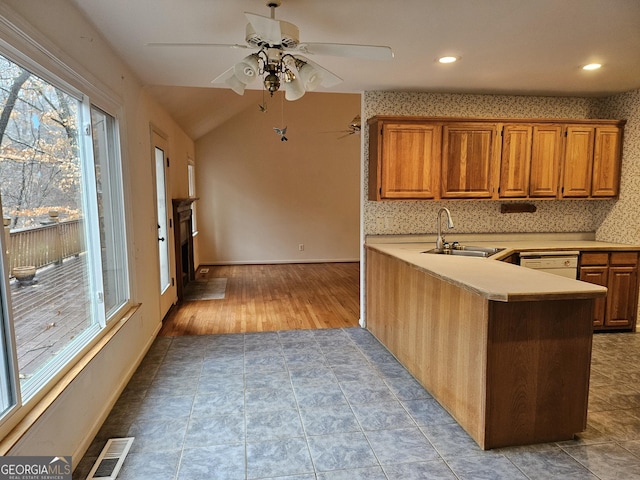 kitchen with kitchen peninsula, vaulted ceiling, ceiling fan, sink, and light hardwood / wood-style floors