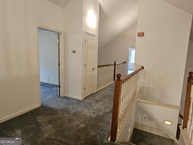 hallway with lofted ceiling and dark colored carpet