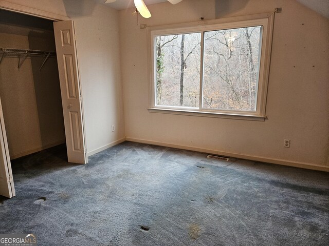 unfurnished bedroom with dark colored carpet, a closet, ceiling fan, and lofted ceiling