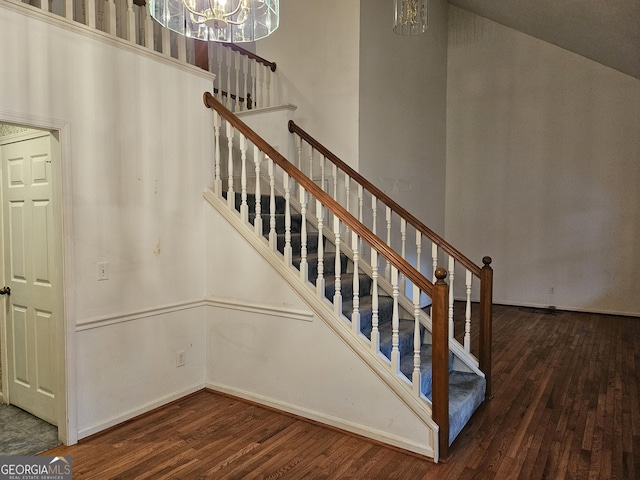 stairs with hardwood / wood-style flooring, a notable chandelier, and vaulted ceiling