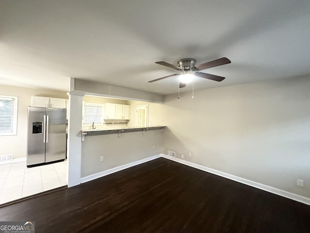 interior space featuring white cabinetry, stainless steel refrigerator with ice dispenser, kitchen peninsula, light hardwood / wood-style floors, and a breakfast bar