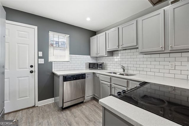 kitchen with gray cabinetry, sink, decorative backsplash, appliances with stainless steel finishes, and light wood-type flooring