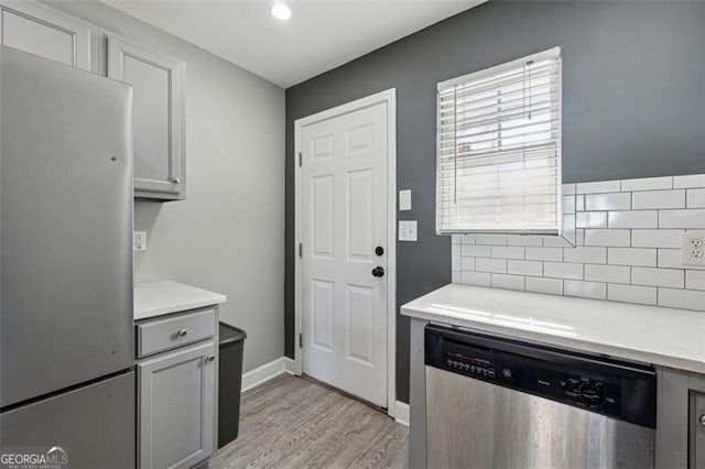 kitchen featuring gray cabinetry, decorative backsplash, light wood-type flooring, and stainless steel appliances