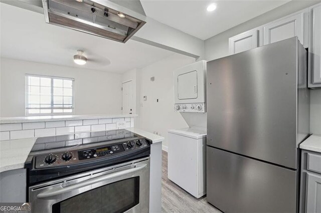 kitchen with light hardwood / wood-style flooring, backsplash, gray cabinets, stacked washer and clothes dryer, and appliances with stainless steel finishes