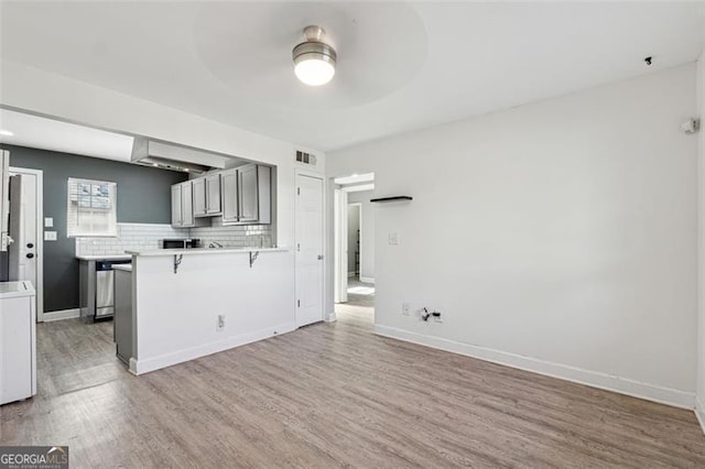 kitchen featuring a breakfast bar, ceiling fan, decorative backsplash, wood-type flooring, and washer / clothes dryer