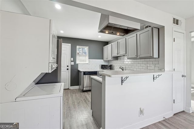 kitchen featuring kitchen peninsula, a kitchen bar, light wood-type flooring, gray cabinetry, and stainless steel appliances