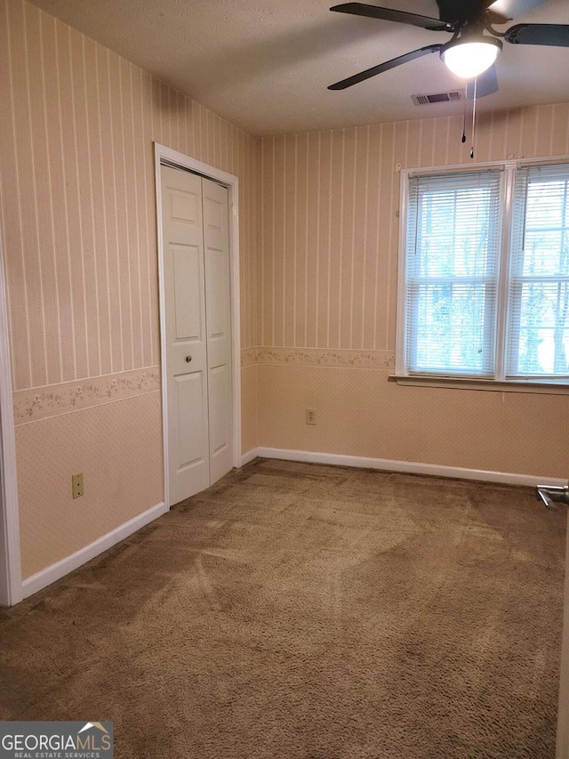 unfurnished bedroom with carpet flooring, ceiling fan, a textured ceiling, and a closet