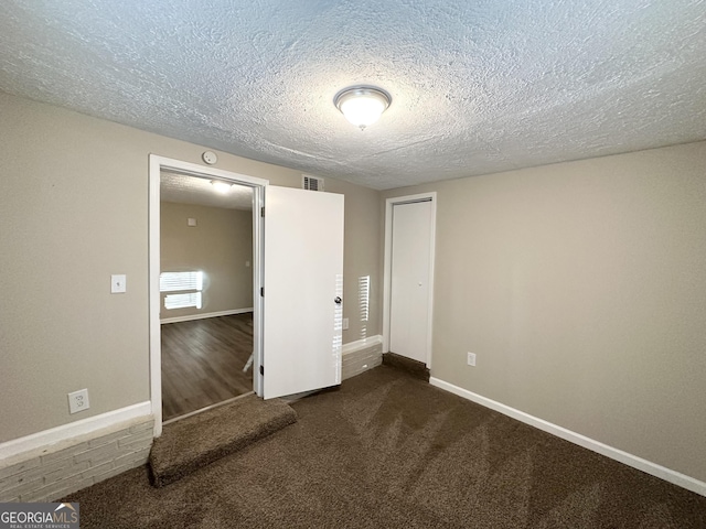 empty room with dark carpet and a textured ceiling