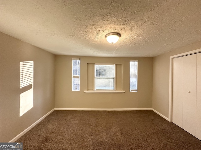 unfurnished bedroom featuring dark colored carpet, a textured ceiling, and a closet