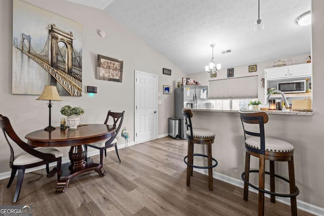 kitchen featuring white cabinetry, light hardwood / wood-style flooring, kitchen peninsula, vaulted ceiling, and a kitchen bar