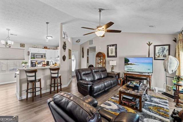 living room with ceiling fan with notable chandelier, a textured ceiling, light hardwood / wood-style floors, and lofted ceiling