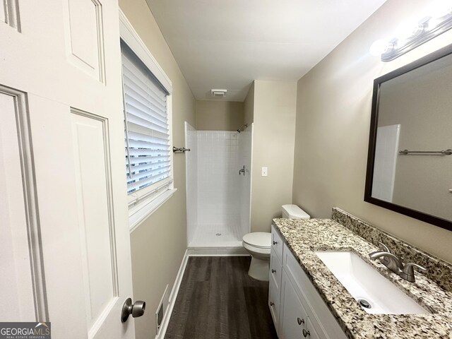 bathroom with a tile shower, hardwood / wood-style floors, vanity, and toilet