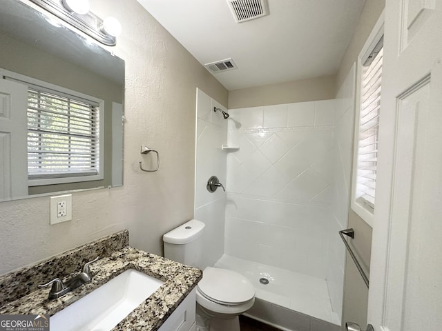 bathroom with tiled shower, vanity, and toilet