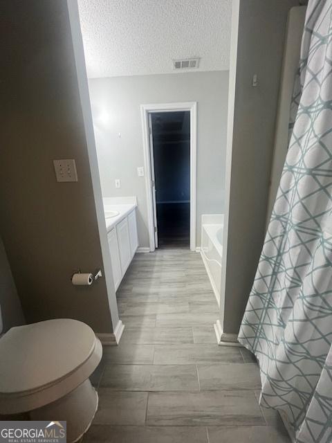 full bathroom with a textured ceiling, vanity, shower with separate bathtub, and toilet