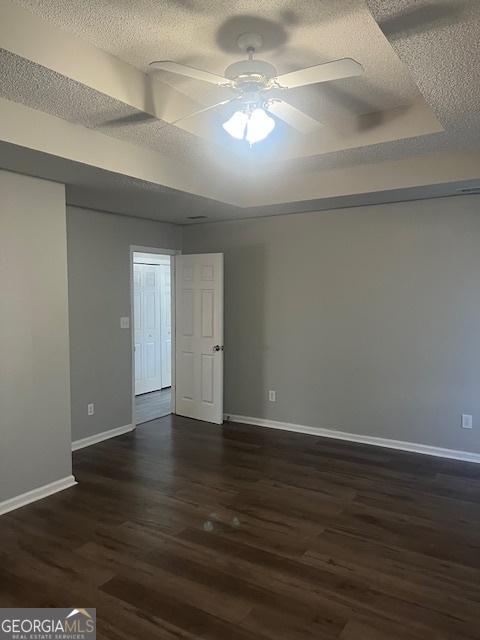 empty room with a textured ceiling, a tray ceiling, ceiling fan, and dark wood-type flooring