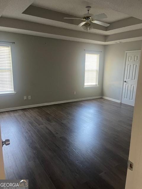 spare room with dark hardwood / wood-style flooring, a raised ceiling, a wealth of natural light, and ceiling fan