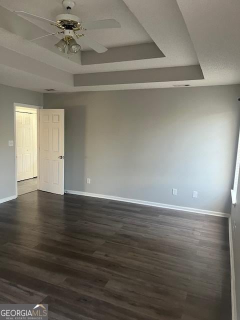 unfurnished room with a tray ceiling, ceiling fan, and dark wood-type flooring